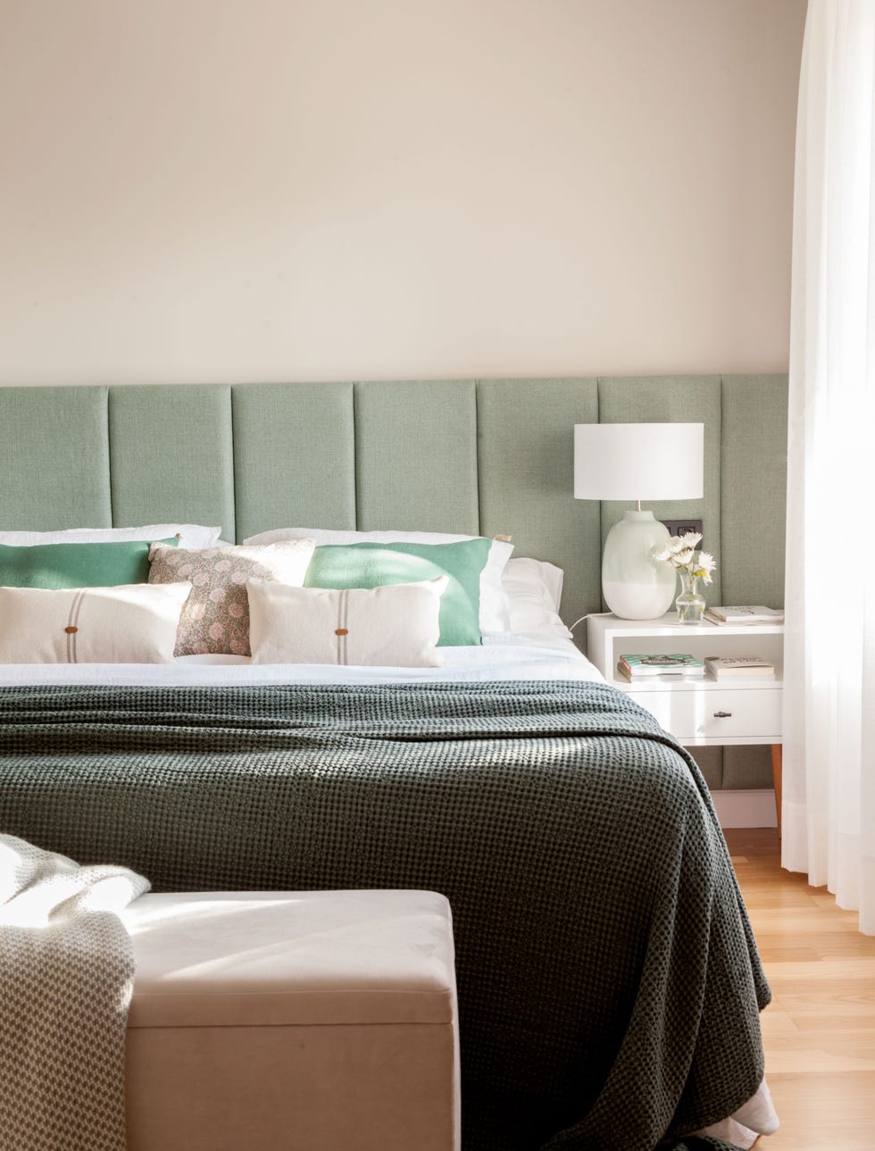cama con cabecero tapizado en verde y banco de terciopelo a los pies