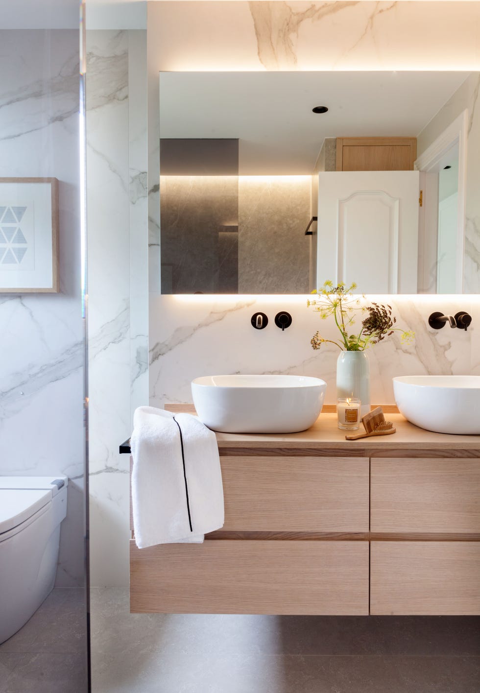 baño con paredes de mármol y mueble suspendido de madera