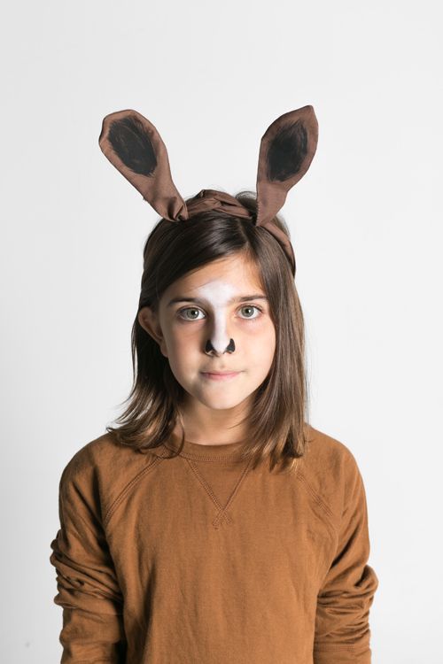 little girl wearing a brown shirt and horse makeup in head wrap folded like horse ears