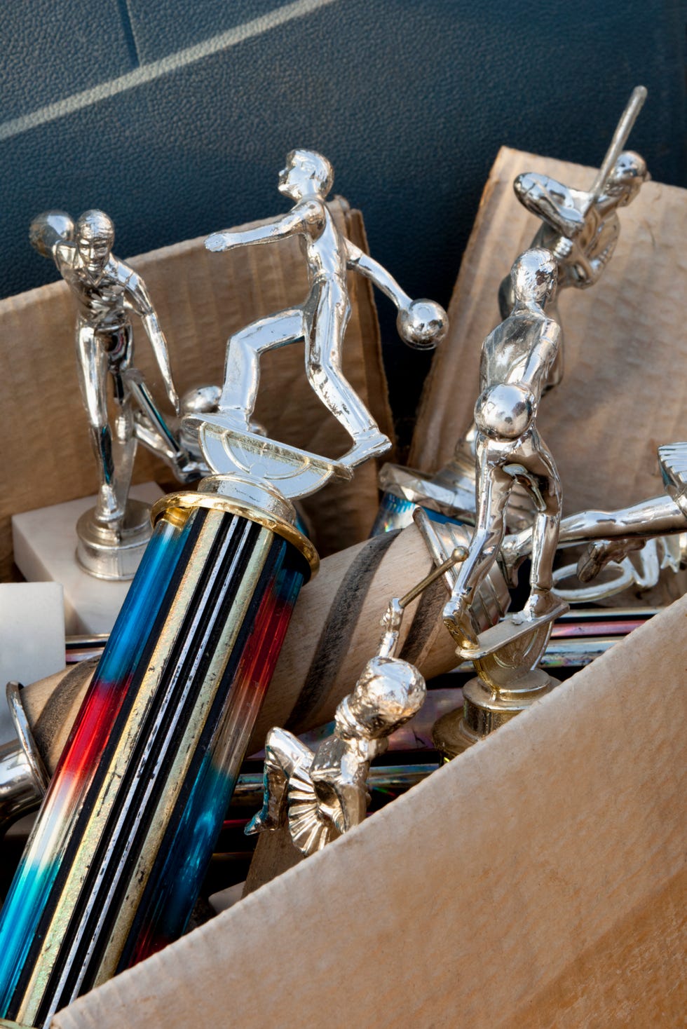 collection of old trophies in a cardboard box. bowling and baseball trophies. box of abandoned relics found in an attic.