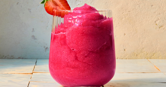 glass with bright pink tropical slushie drink and strawberry garnish
