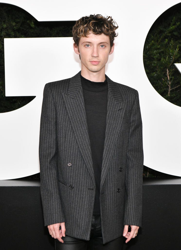 Troye Sivan wears a gray striped suit over a black sweater on the red carpet