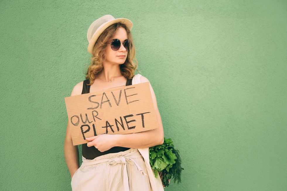 beautiful blonde girl showing save our earth drawing on the brown carton paper over green background