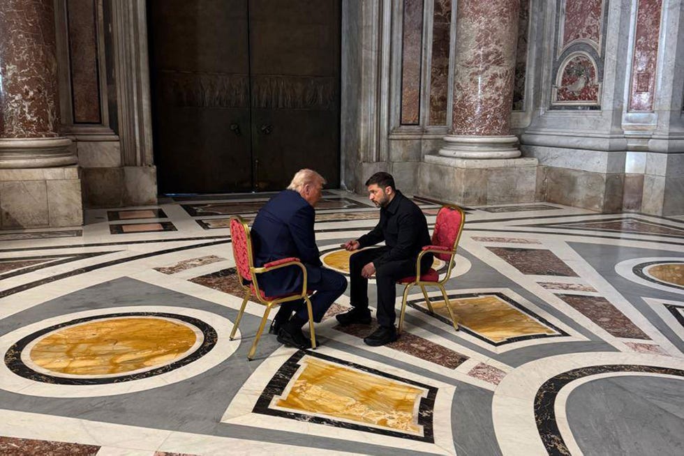 two individuals seated in chairs engaged in conversation in a grand room
