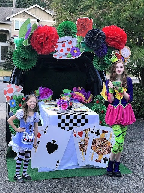 a car decked out for trunk or treat in an alice in wonderland theme with oversize playing cards, a checkerboard table runner and tea cups