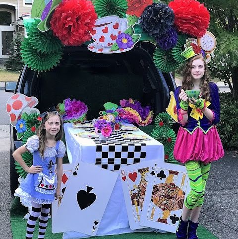 a car decked out for trunk or treat in an alice in wonderland theme with oversize playing cards, a checkerboard table runner and tea cups