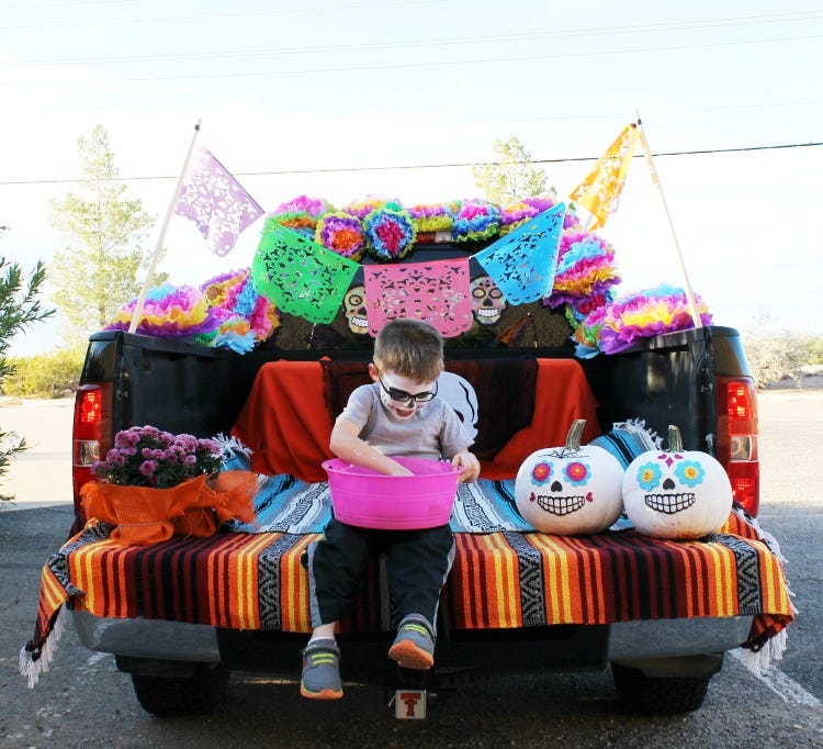 little boy dressed in day of the dead face paint sitting on the back of a truck trunk decorated in a day of the dead style theme trunk or treat