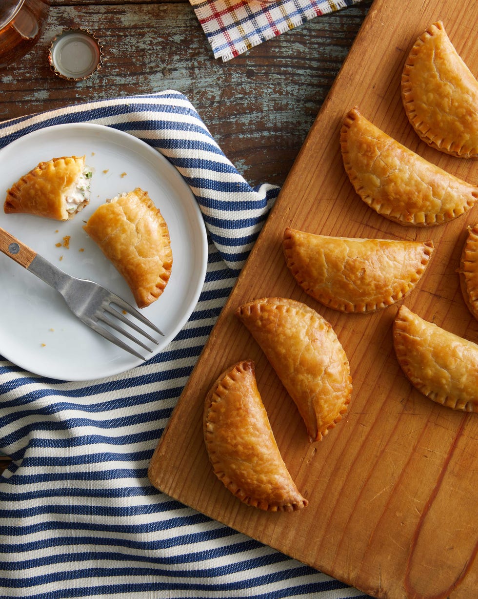 empanadas on a board with one on a plate and some beer near by the one on the plate is broken open empanadas on a board with one on a plate and some beer near by the one on the plate is broken open