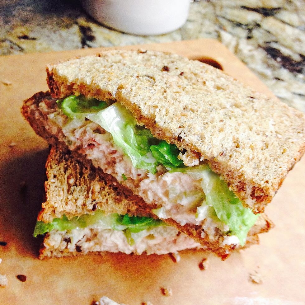 tuna fish and celery sandwich on organic whole wheat bread with gem lettuce cut in half and stacked on a cutting board