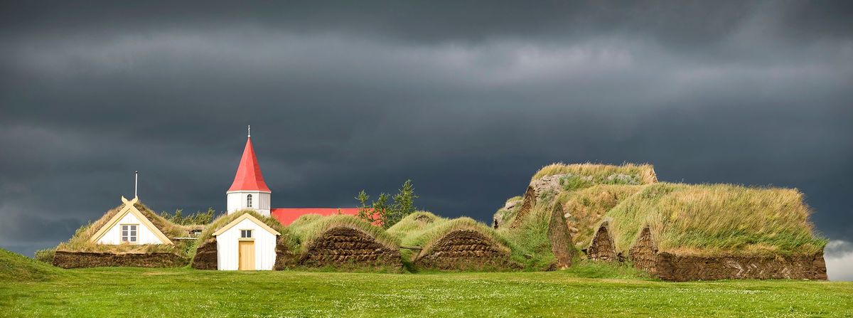 Donkere wolken pakken zich samen boven een turfhuis en een kerk in Glaumbr in IJsland