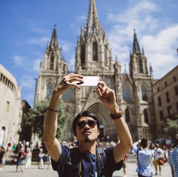 young asian man taking a selfie in front of the barcelona cathedral in spain