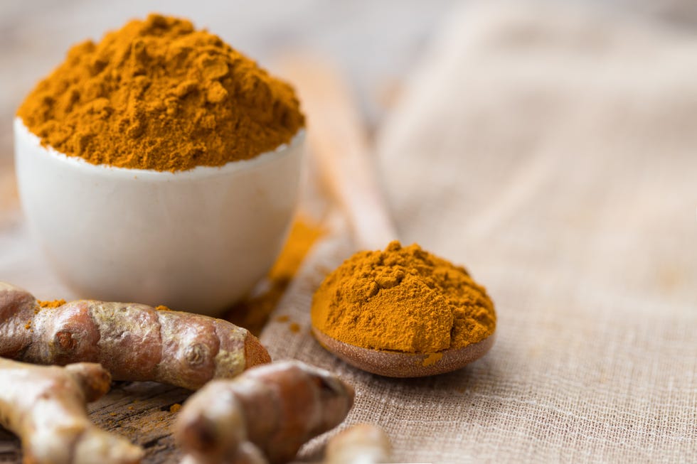 turmeric powder and fresh turmeric in wood bowls on wooden table