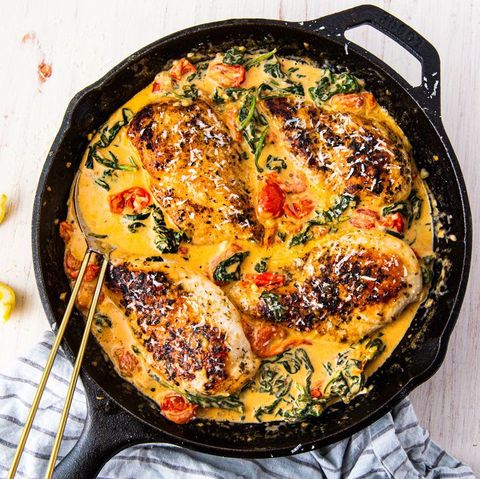 tuscan chicken in yellow cream sauce with spinach and tomatoes in a black cast iron skillet