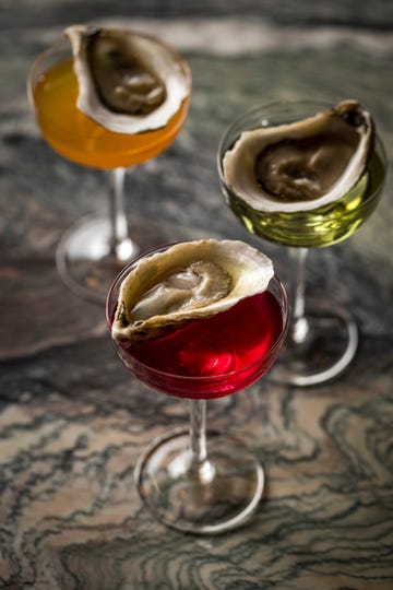 Three cocktail glasses topped with oysters each containing a different colored liquid