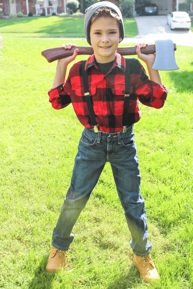 9 or 10 year old boy in lumberjack tween halloween costume with red plaid flannel shirt, suspenders, jeans, boots, toy ax