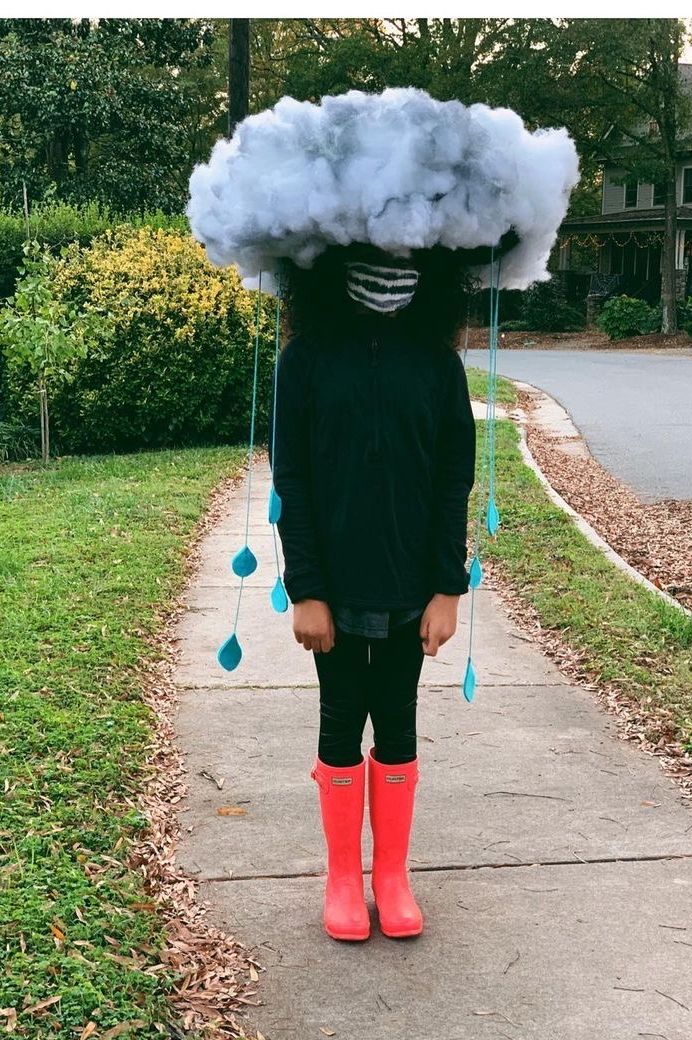 tween girl wearing a storm halloween costume with lit storm cloud hat, black clothes, and neon orange rain boots