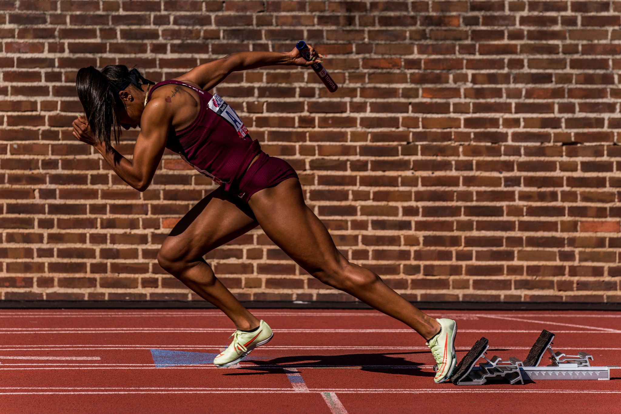 a woman sprints out of blocks in front of a brick background