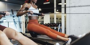 two anonymous fit women rowing at the gym