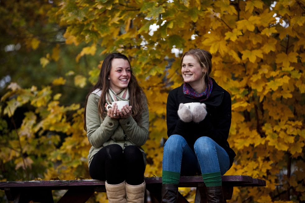 two athletic young women smiling drink coffee surrounded by fall colors in the early morning in idaho