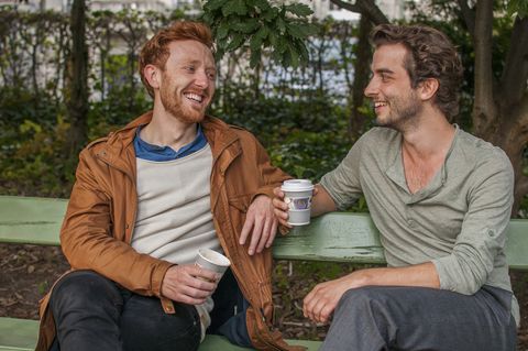two attractive men drinking coffee in the park