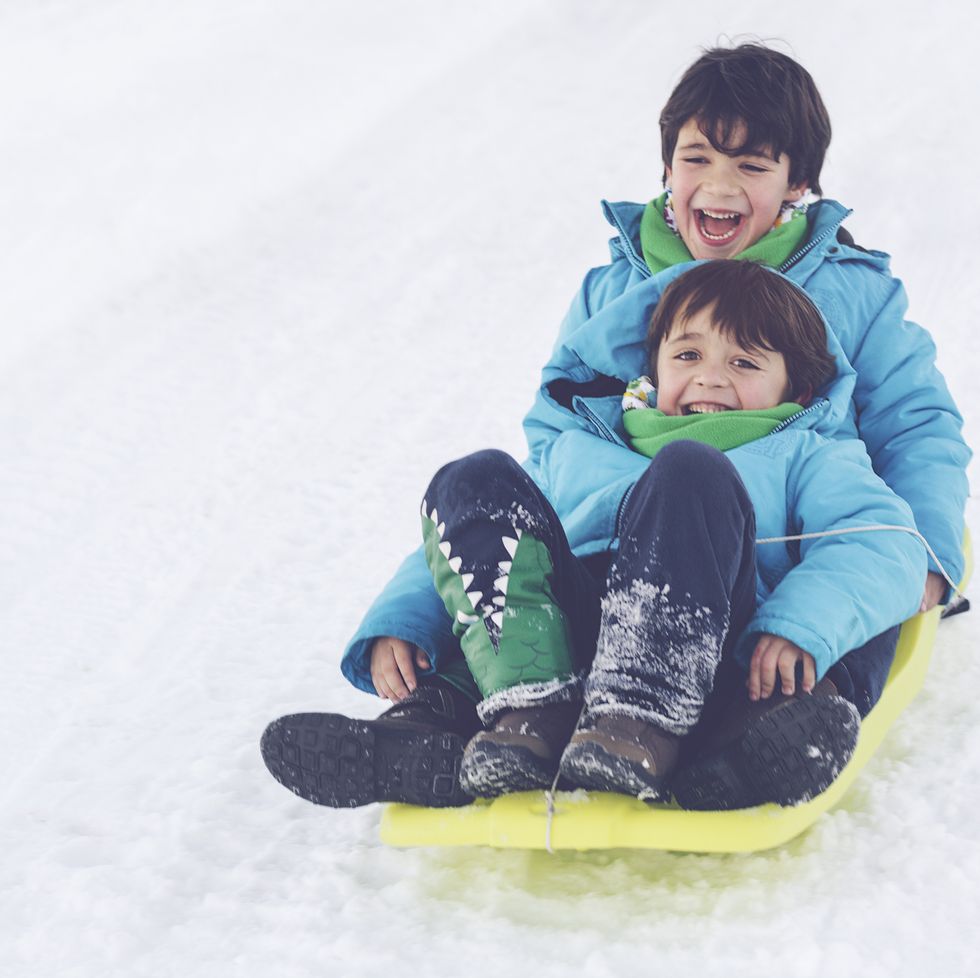 christmas activities  two brothers on toboggan on snow covered hill