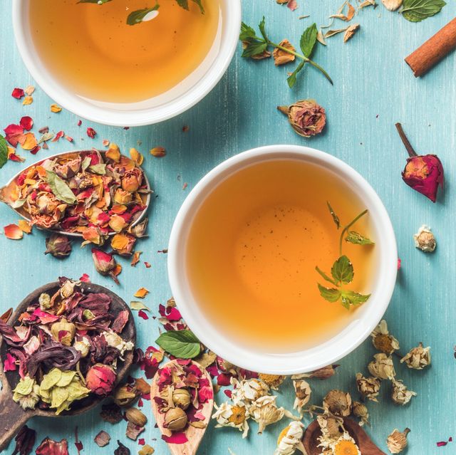 two cups of healthy herbal tea with mint, cinnamon, dried rose, camomile flowers in spoons and man's hand holding spoon