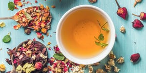 two cups of healthy herbal tea with mint, cinnamon, dried rose, camomile flowers in spoons and man's hand holding spoon