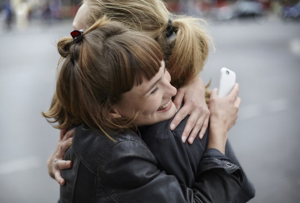 two female friends with cell phone hugging