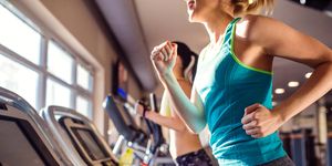 Two fit women running on treadmills in modern gym
