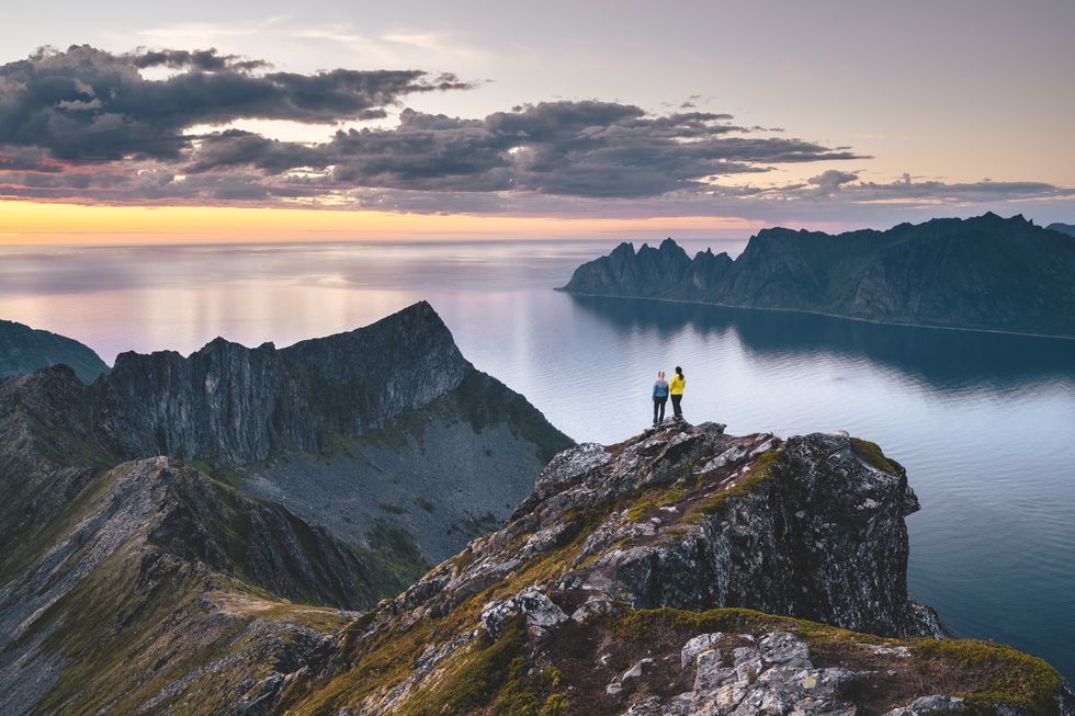 two friends admiring the sunset from top of a high cliff in northern norway