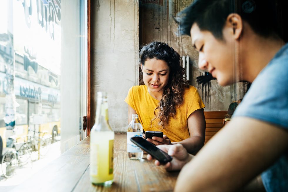 Two Friends Using Smartphones While Waiting For Food