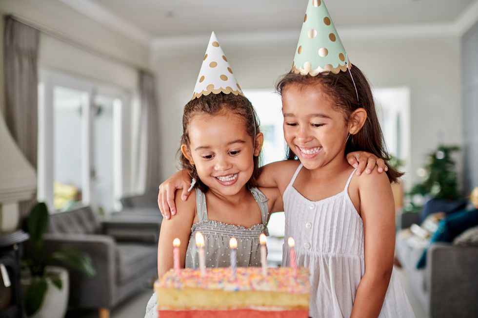 two sisters in party hats about to blow out birthday cake candles