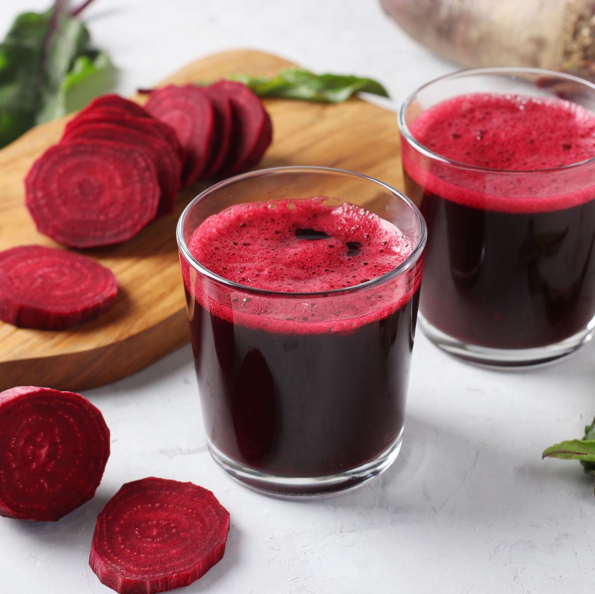 two glass of fresh beetroot juice and chopped beet on wooden board on gray background closeup