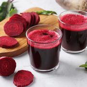 two glass of fresh beetroot juice and chopped beet on wooden board on gray background closeup
