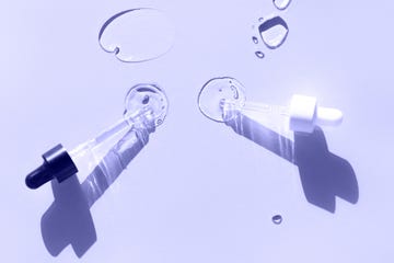 two glass pipettes spilling transparent moisturizing lotion on pastel violet background macro photography demonstrating very peri color of 2022 year