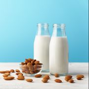 two glass reusable bottles with almond milk almond nuts lie on a white wooden table and a blue background