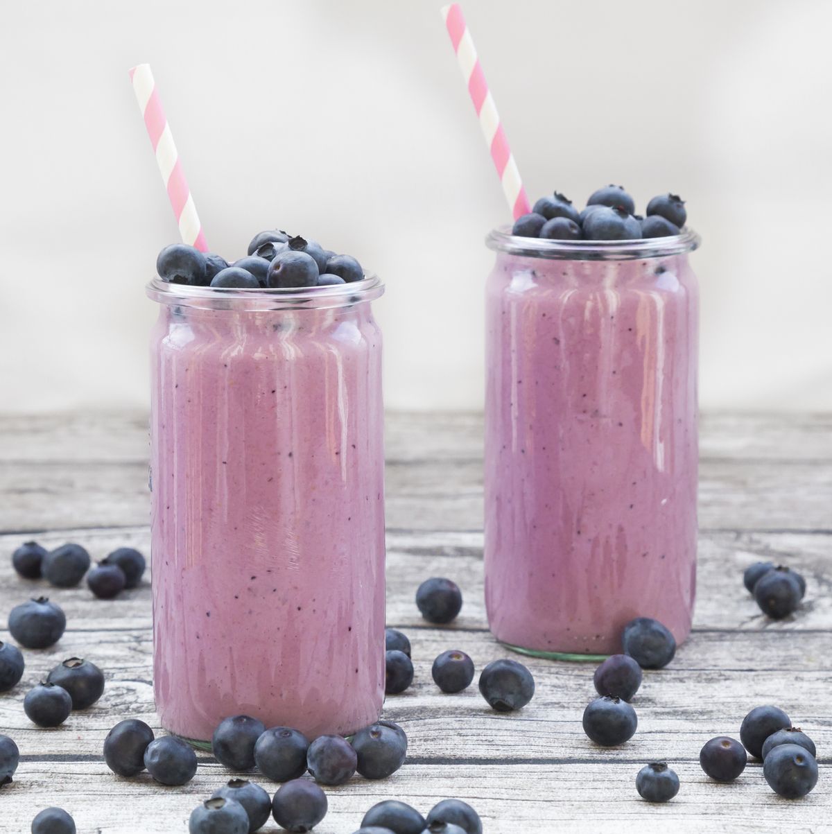 two glasses of blueberry smoothie and blueberries on wood