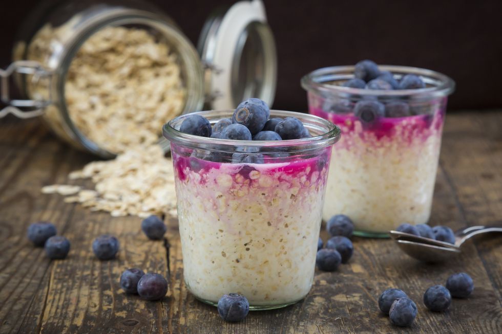two glasses of overnight oats with blueberries and berry juice on wood