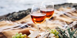 two glasses of wine and summer fruits on the beach, sea and landscape in background, summer picnic, idea for outdoor weekend activity