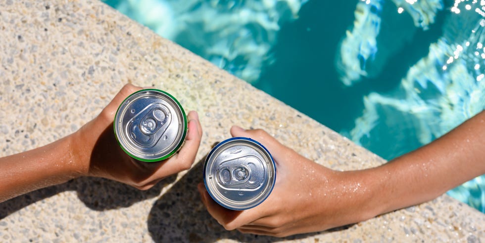 two hands hold cans of cold drink in the pool on a hot day the concept of vacation in a friendly company