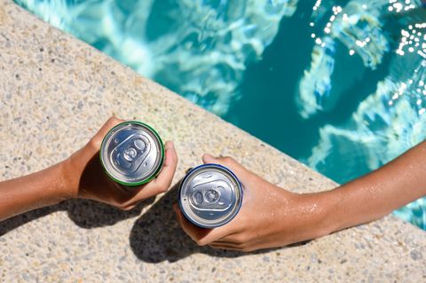 two hands hold cans of cold drink in the pool on a hot day the concept of vacation in a friendly company