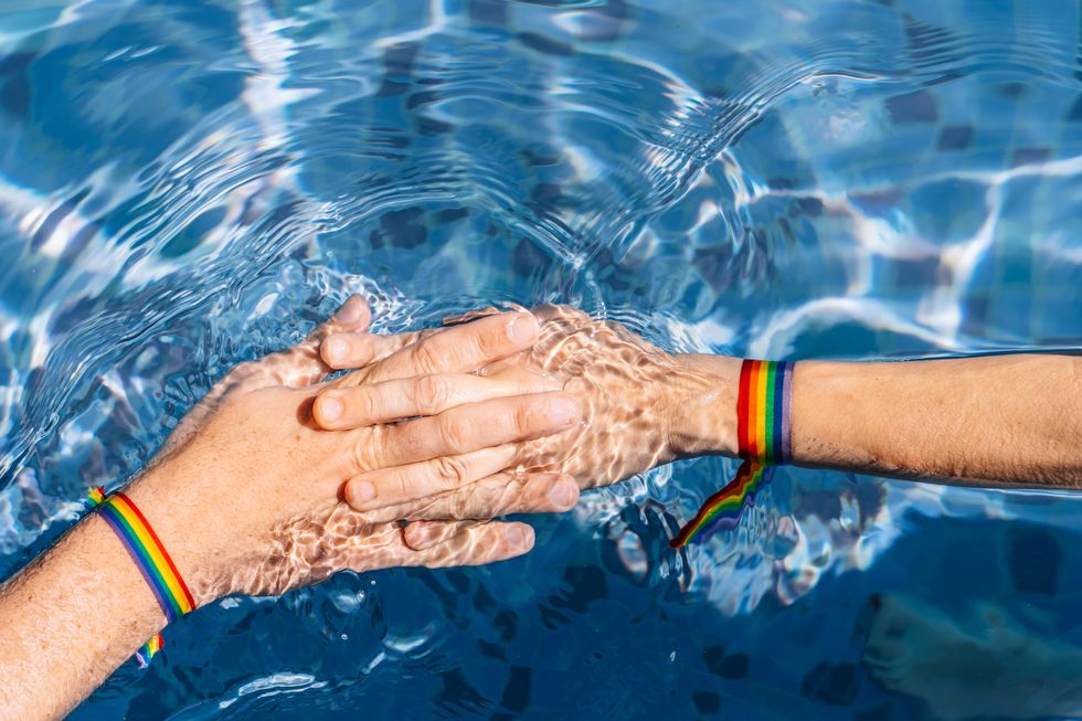 two hands holding together on the water of a pool with a rainbow flag lgtb concept