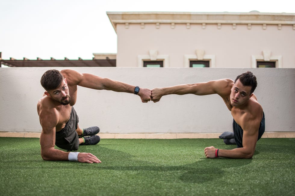 Two handsome shirtless men giving fist bump after successful workout at rooftop gym.