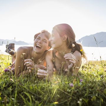 two happy female friends lying on a meadow in the mountains, achenkirch, austria