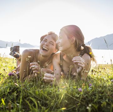 two happy female friends lying on a meadow in the mountains, achenkirch, austria