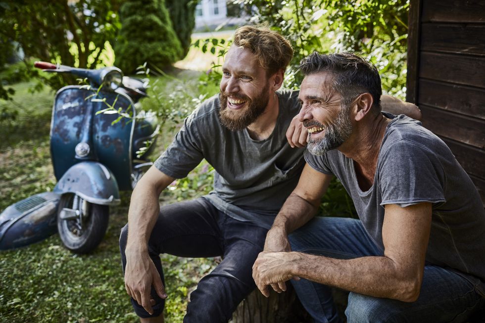 two happy men sitting together at garden shed with old motor scooter in background
