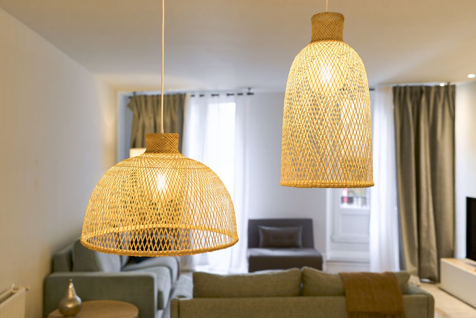 two lamps hanging from the ceiling woven in yellow thread, lit at different levels in the background a living room with several furniture and cushions, with curtains and wall in white color