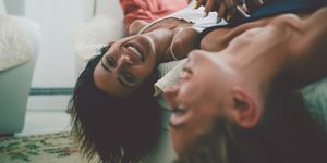 two laughing sensual females lying on sofa and holding hands upside down