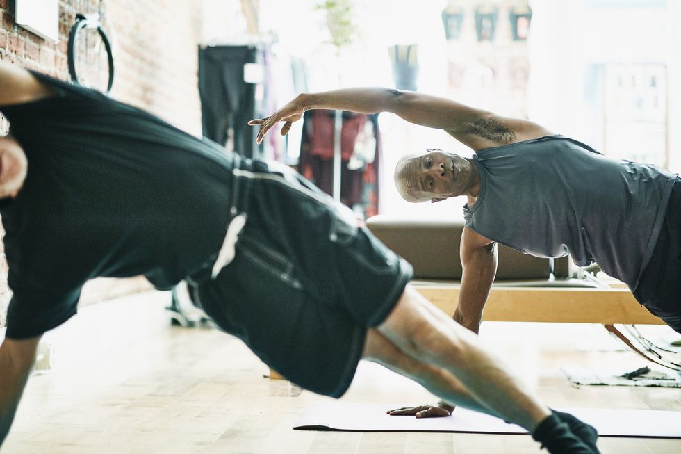 two mature men performing side plank on mat during pilates class in exercise studio