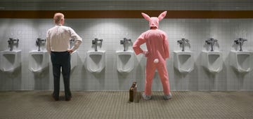 two men standing at urinal, one in rabbit costume, rear view digital composite